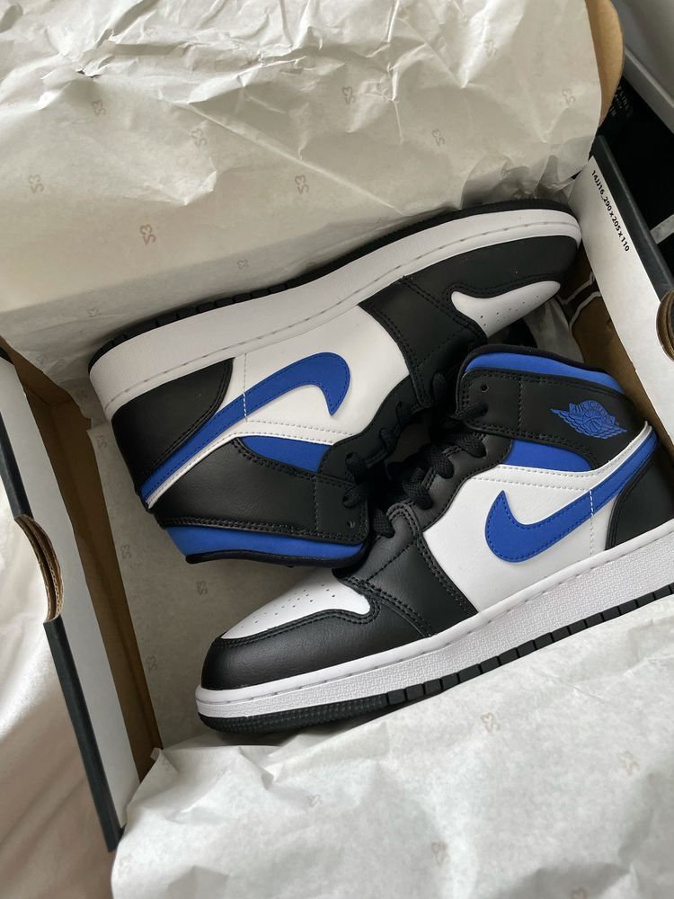 Jordan 1 Mid Black Racer Blue in hand – blauwe enkelkraag, zwarte panelen en witte zool helder in beeld onder daglicht