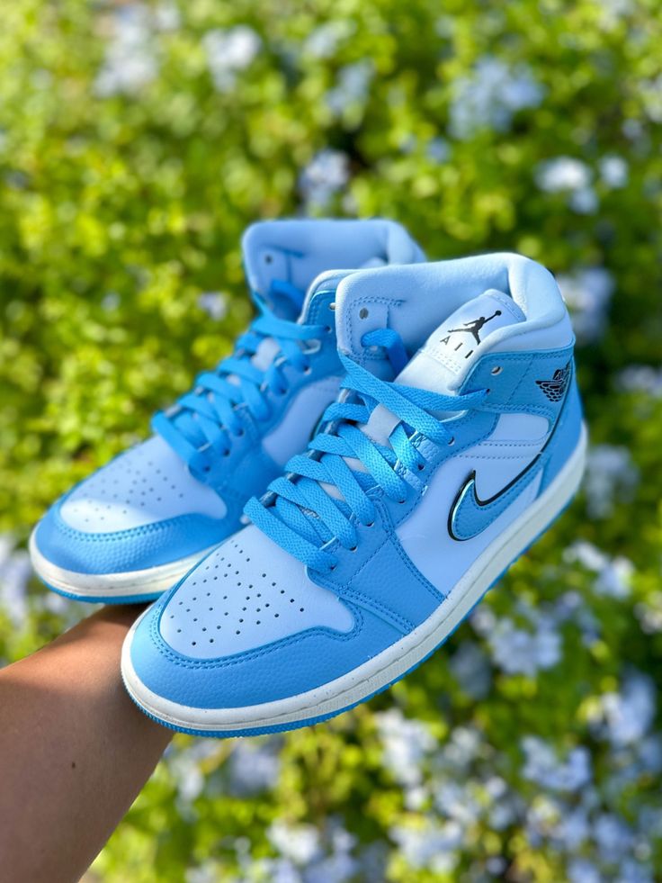 In-hand shot van Air Jordan 1 Mid Ice Blue – zachte blauwe panelen, witte zool en zwarte branding in daglicht zichtbaar