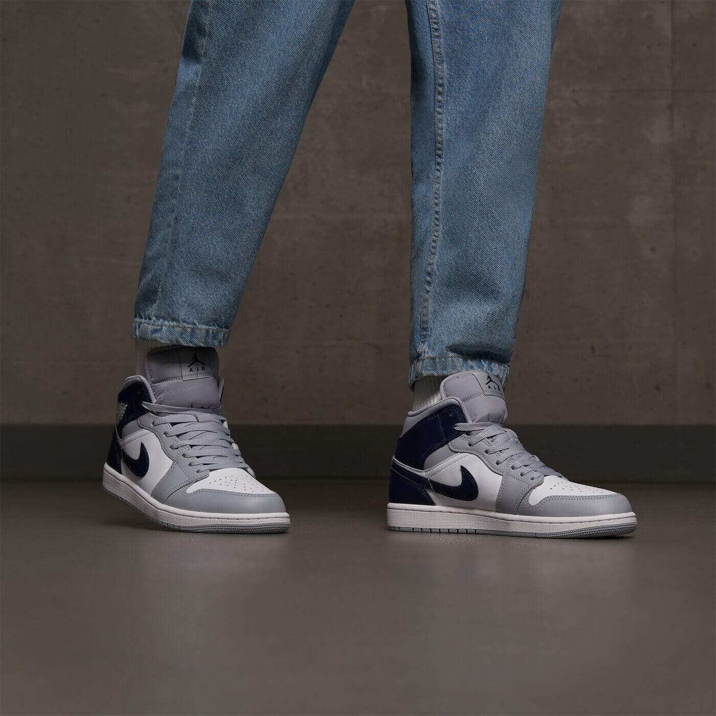 AJ1 Mid Wolf Grey Midnight Navy on‑feet – gedragen met lichtgrijze cargopants; urban street-style look die geliefd is onder Gen Z sneakerfans