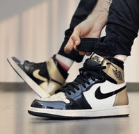 In hand shot van de Jordan 1 Golf met gouden hiel en zwart gelakte afwerking – premium patent materiaal en sportieve performance uitstraling