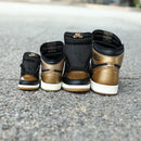 Achteraanzicht van twee paren Jordan 1 High Black Metallic Gold op straat en zicht op het glanzende leer en het contrast met de middenzool