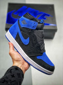 In hand shot van de Air Jordan 1 Royal Reimagined met zicht op zwarte Swoosh, blauwe hiel en OG-high silhouet – retro feel met premium suède textuur