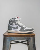 Flatlay van de sneaker en OG-box – de mix van grijs, wit en sail zorgt voor een subtiele maar sterke retro-uitstraling

