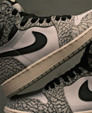 In hand shot van de Air Jordan 1 Cement met close-up op de textuur van de print en het zwart-witte contrast – OG DNA in modern detail gevangen