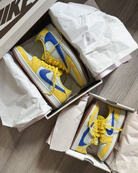 Detail van Air Jordan 1 Low OG Travis Scott Canary (SKU DZ4137‑700) met reversed Racer Blue Swoosh en Cactus Jack tonglabel