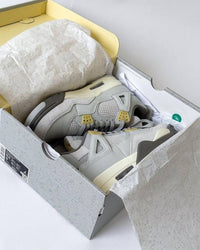 Air Jordan 4 Craft Photon Dust DV3742-021 in hand vastgehouden met zicht op geribbelde hielclip, zachte overlays en grijze ton-sur-ton afwerking