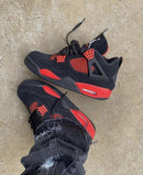 Jordan 4 Red Thunder CT8527-016 half uit doos geschoven met zicht op het matte zwart suède en de dieprode tonginzet onder kunstlicht