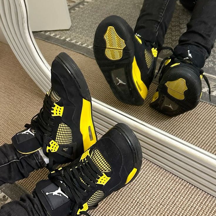 Air Jordan 4 Thunder 2023 DH6927-017 gedragen met losvallende jeans, zichtbaar in beweging met felgele middenzool en zwarte cages