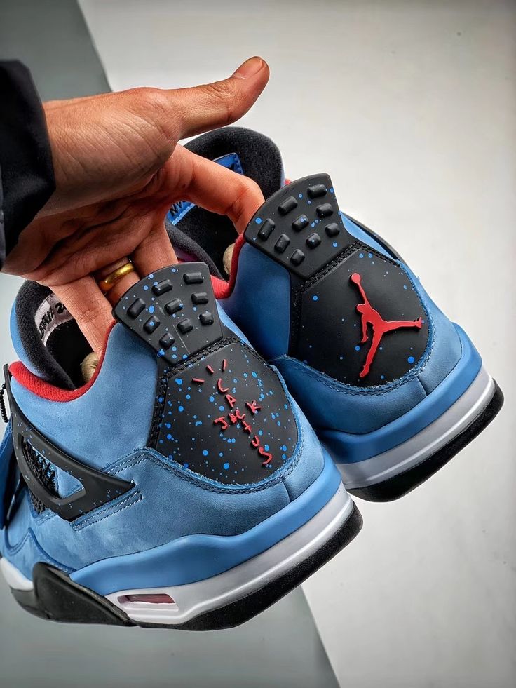 Air Jordan 4 Cactus Jack 308497-406 vastgehouden aan de hiel, met zicht op de gespikkelde heel tab, Cactus Jack branding en blauwe upper in zonlicht