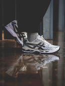 Close-up van de ASICS Gel Kayano 14 Cream Black Metallic Plum gedragen op straat – reflecterende overlays en plumkleurige accenten, model 1202A056 118

