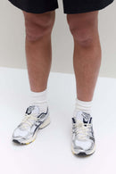 Bovenaanzicht van de sneaker met JJJJound-logo op de tong, strak vetersysteem en mesh overlays in wit en donkerblauw

