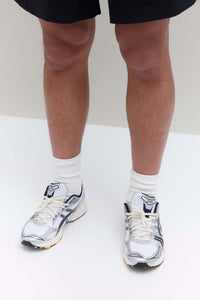 Bovenaanzicht van de sneaker met JJJJound-logo op de tong, strak vetersysteem en mesh overlays in wit en donkerblauw

