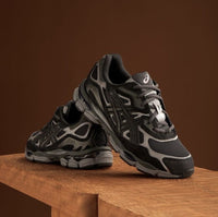 Bovenaanzicht van de ASICS GEL-NYC Black Graphite Grey zicht op tonglogo, donkere veters en strakke lijnen via Snrkickz