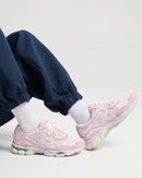 On-feet shot van de ASICS Gel-NYC Cream Rose Water gedragen met navy pants op een witte ondergrond, gericht op detailgerichte mobile zoekopdrachten