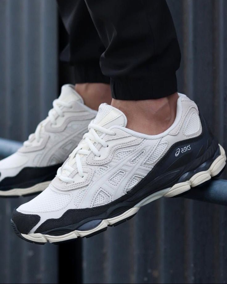 On-feet shot van de ASICS Gel-NYC White Smoke Grey met zwarte broek op straat, perfect voor zoekopdrachten naar urban styling en draagmomenten