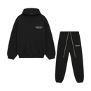 Flatlay van de volledige Fear of God Essentials FW24 set in zwart met wit logo, bestaande uit hoodie en sweatpants tegen witte achtergrond