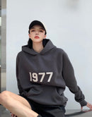 Achterzijde van de Essentials 1977 Hoodie Iron – cleane rugzijde met lichtgrijze tint en subtiel label onder de capuchon via Snrkickz
