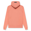 Model wearing Fear of God Essentials FW22 Coral Hoodie highlighting oversized fit, bright coral color and relaxed premium streetwear style.