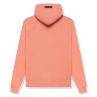 Model wearing Fear of God Essentials FW22 Coral Hoodie highlighting oversized fit, bright coral color and relaxed premium streetwear style.