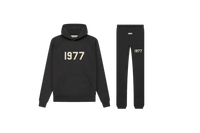Studiofoto van de Fear of God Essentials IRON 1977 Full Set bestaande uit hoodie en sweatpants in zwarte kleur met 1977 opdruk