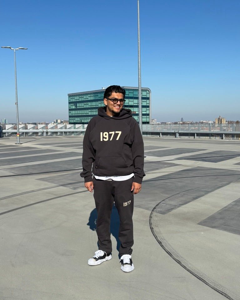 Close-up van de Fear of God Essentials IRON 1977 hoodie en pants gedragen in een open ruimte, met zichtbare oversized fit