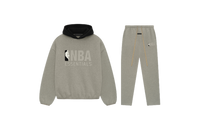 Fear of God Essentials NBA Warm Heather Full Set met hoodie en joggers in warme heathergrijze tint, voorzien van NBA Essentials-logo en contrasterende zwarte capuchon voor een moderne sportieve uitstraling