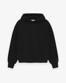 Model wearing Fear of God Essentials SS25 Jet Black Hoodie highlighting oversized fit, tonal logo print and clean modern streetwear style.