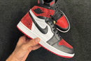 In hand shot van de Jordan 1 High Ruby met zwart Wings-logo en robijnrode hiel – premium materialen en iconisch design vastgelegd in detail