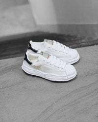 Maison Mihara Yasuhiro Blakey OG Sole Leather Low White (SKU A06FW702-WHT) – model draagt deze Regular fit sneaker met tapered denim voor een avant-garde streetwear look