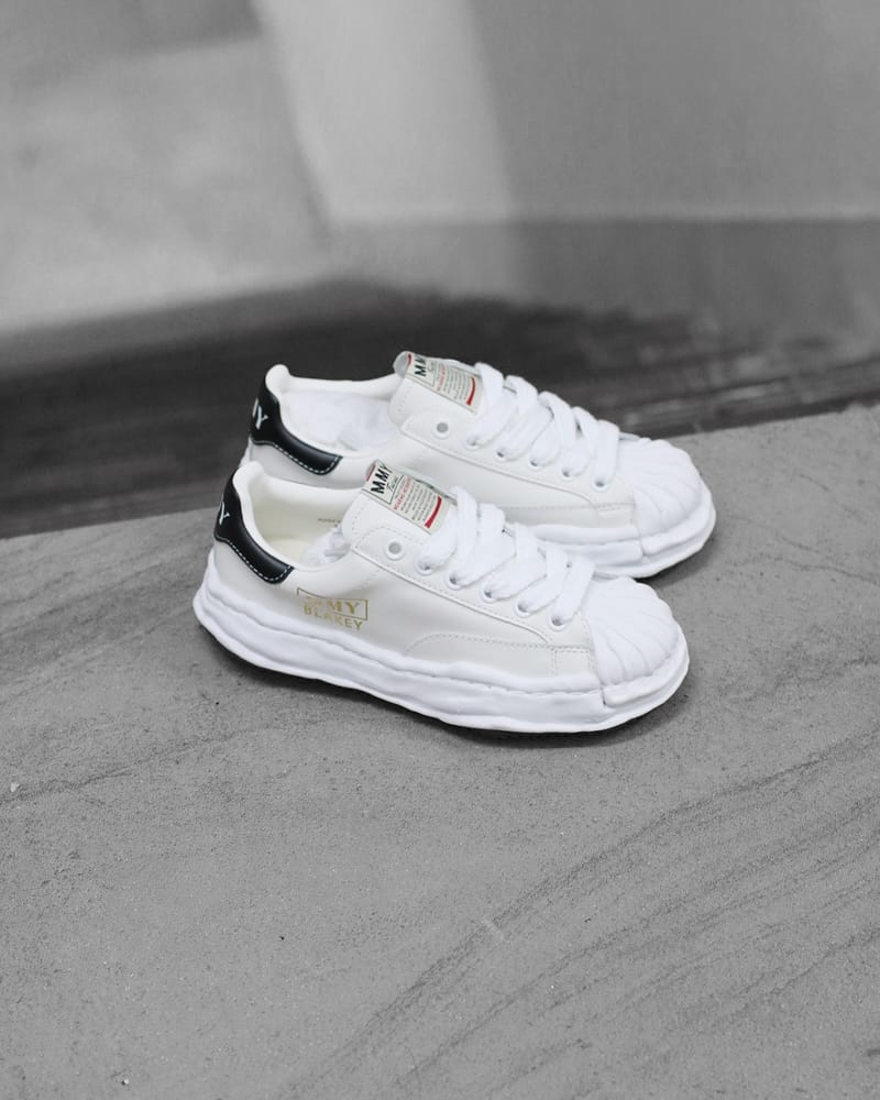Maison Mihara Yasuhiro Blakey OG Sole Leather Low White (SKU A06FW702-WHT) – model draagt deze Regular fit sneaker met tapered denim voor een avant-garde streetwear look