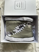A11FW701-GRN Maison Mihara Yasuhiro Peterson 23 OG Sole Canvas High Green – model draagt de high-top canvas sneaker met tapered denim voor een avant-garde streetwear look 