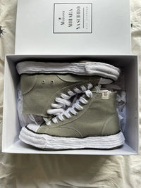 A11FW701-GRN Maison Mihara Yasuhiro Peterson 23 OG Sole Canvas High Green – model draagt de high-top canvas sneaker met tapered denim voor een avant-garde streetwear look 