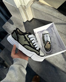 Maison Mihara OG Sole Khaki sneaker close-up in doos, vastgehouden in direct zonlicht met zichtbare canvasstructuur