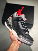 Hand houdt de Air Jordan 3 Black Cement omhoog voor een zwarte doos met rood Jumpman-logo, zichtbare details van de elephant print en demping in de hiel