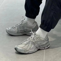 In-hand view van de New Balance 1906A Concrete Silver Metallic. De combinatie van matte en glanzende materialen zorgt voor een futuristische, maar draagbare sneakerrelease.

