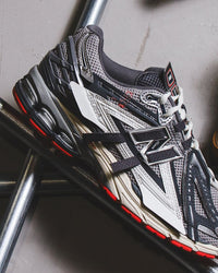 In-hand view van de New Balance 1906A in Slate Grey en Drift Red. Een opvallende uitvoering die retro performance combineert met moderne materialen en uitgesproken kleuren.

