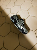 Close-up van het metallic bovenwerk van de New Balance 1906L Silver Black. Het contrast tussen het zilveren mesh en de zwarte overlays creëert een uitgesproken en technisch silhouet.

