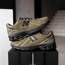 Onderzijde van de New Balance 1906R Camo Olive met robuuste zool en N-ERGY demping. De kleuren in het profiel versterken het rugged, utilitaire uiterlijk van de sneaker.

