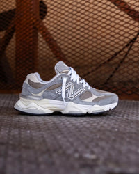 New Balance 9060 Slate Grey met Arid Stone details gestyled in industriële setting met mesh-achtergrond