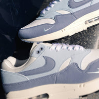 Close-up van Nike Air Max 1 Light Armory Blue gedragen op straatstenen, met focus op materialen en Air-unit voor streetwear styling