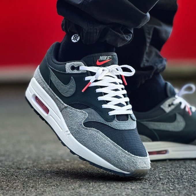 In-hand shot van de Air Max 1 ’87 Dark Smoke Grey met ruwe textuur, zwarte accenten en zichtbare Air-unit
