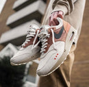 Lifestyle close-up met beide sneakers gedragen in een stedelijke setting, waarbij de aardse kleuren harmoniëren met het lijnenspel van de achtergrond