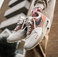 Lifestyle close-up met beide sneakers gedragen in een stedelijke setting, waarbij de aardse kleuren harmoniëren met het lijnenspel van de achtergrond