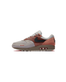 Zijaanzicht van de Air Max 1 Amsterdam met baksteenrode tinten, suède overlays en een minimalistische, cleane achtergrond die het silhouet versterkt