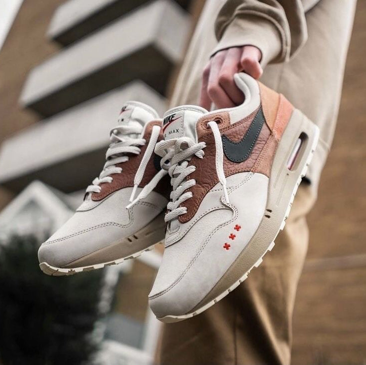 Lifestyle close-up met beide sneakers gedragen in een stedelijke setting, waarbij de aardse kleuren harmoniëren met het lijnenspel van de achtergrond