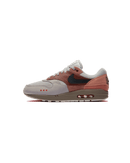 Zijaanzicht van de Air Max 1 Amsterdam met baksteenrode tinten, suède overlays en een minimalistische, cleane achtergrond die het silhouet versterkt