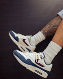 In-hand shot van de Nike AM1 Coconut Milk met zachte suède, retro colorblocking en zichtbare Air-unit