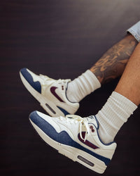 In-hand shot van de Nike AM1 Coconut Milk met zachte suède, retro colorblocking en zichtbare Air-unit