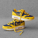 Sfeerbeeld van de sneaker in gedempt licht op betonnen vloer, waarbij de gele tonglabel en navy Swoosh sterk contrasteren