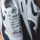 Sneakers strak gepositioneerd tegen beige achtergrond met nadruk op de gewatteerde tong, zichtbare Air-unit en donkere toebox